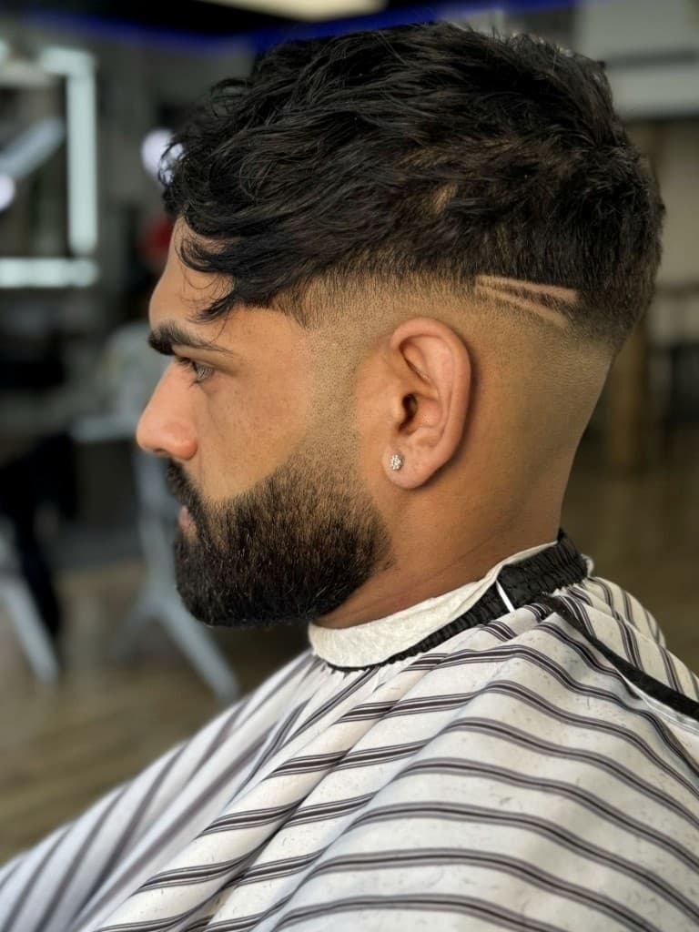 Skin fade with custom slash design and sculpted beard