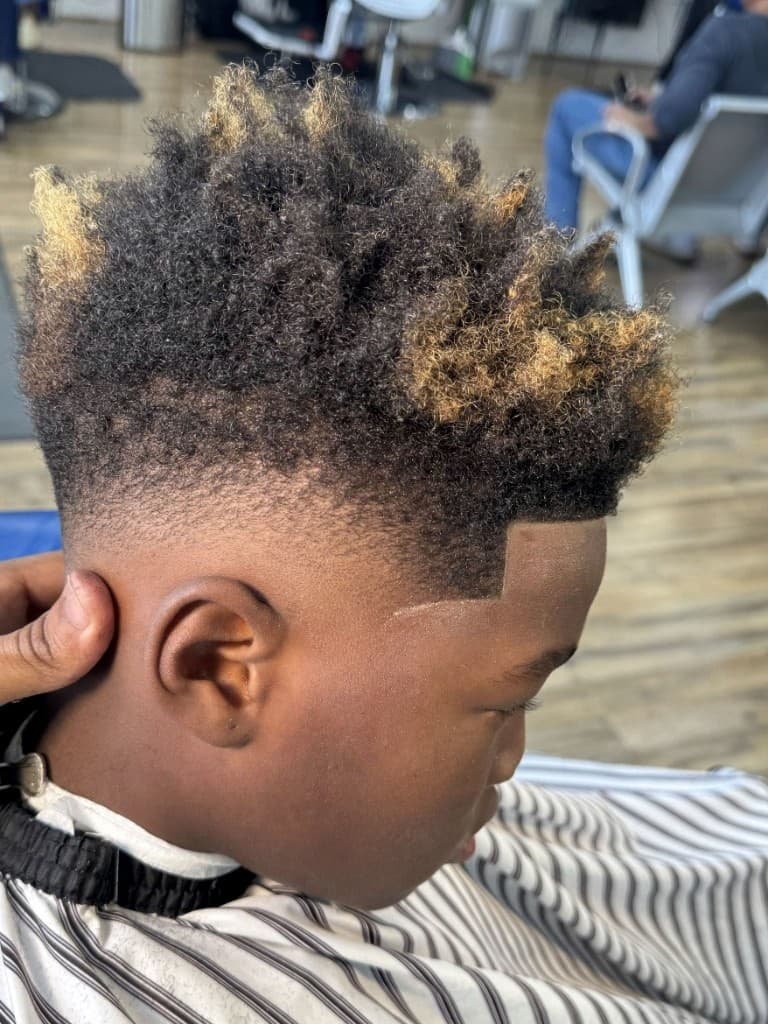 Kid's curly top with skin fade, sharp lineup, and blonde tips