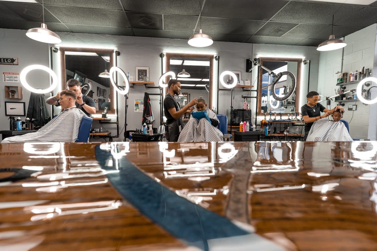 Barbers at work across stations, seen over the epoxy river table at Vanzant